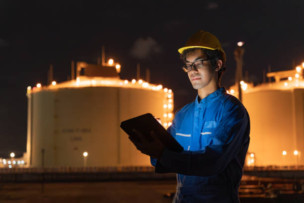 istock Mid adult Asian inspection engineer male working with digital tablet for inspecting process of refinery plant at night. Asian mid adult man wearing safety helmet and uniform holding digital tablet, reading data during inspecting pipeline industry site. 2168300824
