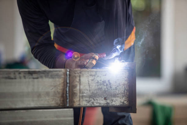 A man is sitting on the ground and working on a metal structure. He is wearing blue jeans and white shoes