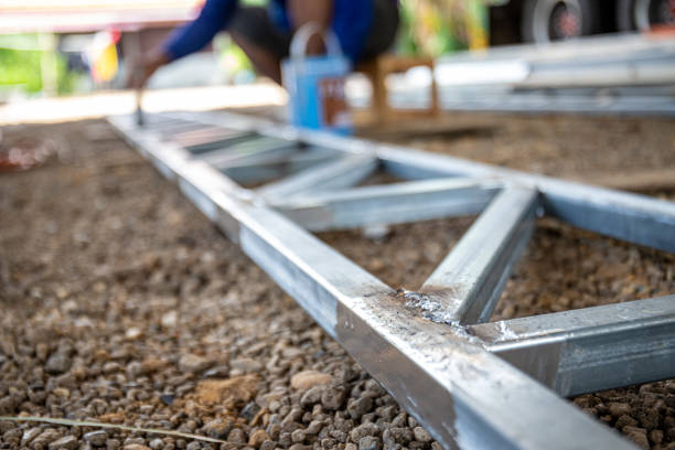 A man is painting a metal structure with a brush. He is wearing a blue shirt and sandals