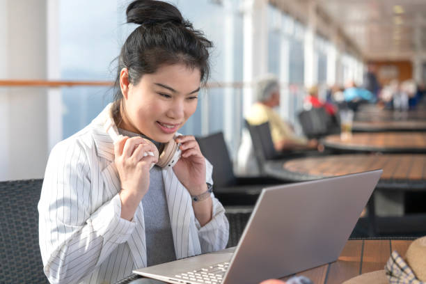 Asia female using laptop working online remotely working from cruise deck while listening music from wireless headphone,freelance asian female woman working online using laptop carefree working leisure working anywhere anytime