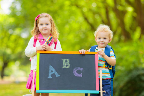 Children happy to be back to school. Preschooler girl and boy with backpack and books at black chalk board learning to write letters and read. Kids at preschool or kindergarten learn the alphabet.