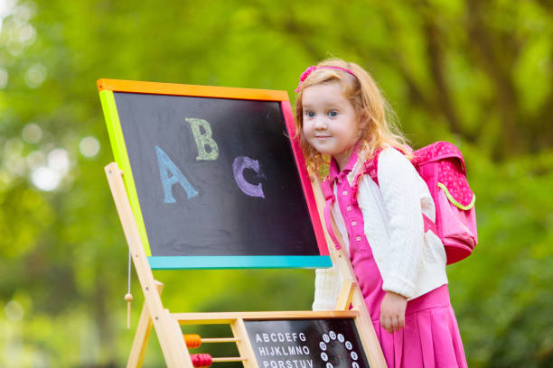 Children happy to be back to school. Preschooler girl and boy with backpack and books at black chalk board learning to write letters and read. Kids at preschool or kindergarten learn the alphabet.