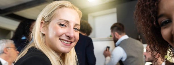 Horizontal banner or header with young blonde caucasian woman looking at camera during work with multiethnic team at the modern office - Coworking concept