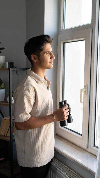 istock teenage man looking out the window with binoculars 2168339044