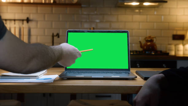 istock Two anonymous men working with laptop computer with green mock up screen on table in the kitchen pointing screen with pen. Co-workers working home office, remote work, technology concept 2168339313