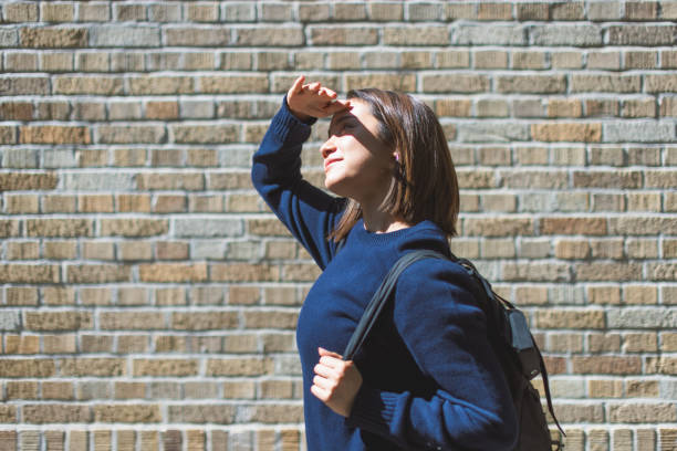 istock Young Woman Shielding Eyes from Sun Against Brick Wall 2168350639