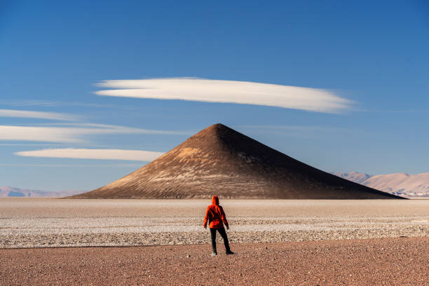 Rear view of a tourist in the volcanic scenery admiring cone-shape mountain against blue sky, Cono de Arita, Salar de Arizaro, Salta province, Puna, Argentina
