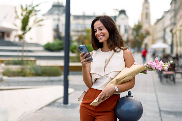 istock Smiling woman checking phone while holding pink flowers 2168360824