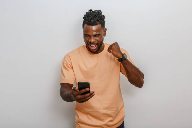 istock Man celebrating success while looking at smartphone in a light-colored top against a neutral background 2168360858