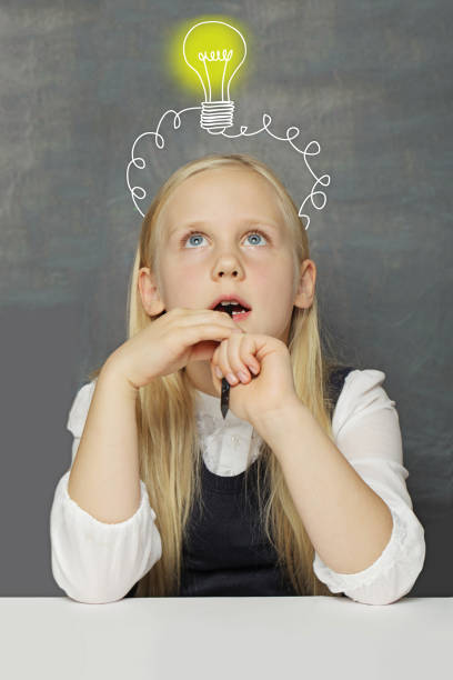 istock Thinking kid schoolgirl with yellow light bulb on school blackboard background. Creativity, education and idea concept 2168364130