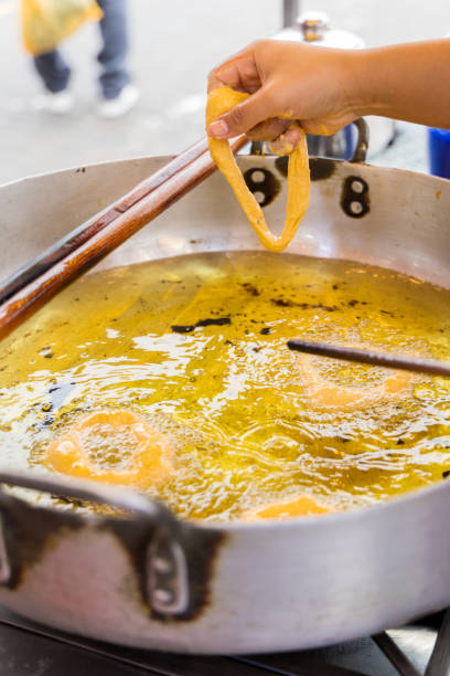 A woman is cooking picarones in a pan. The food is being cooked on a stick