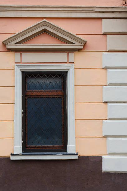 A pair of vintage-style windows frames set against a white wall. One window is slightly open, revealing beige curtains inside. The symmetry and classic design elements add a touch of traditional charm to the facade.