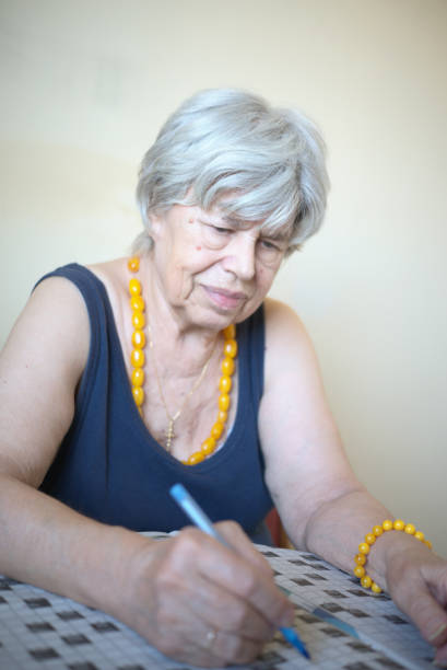 Portrait of an elderly woman solves a crossword puzzle at home.