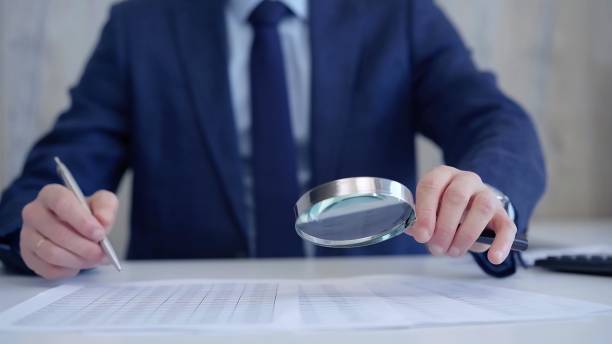 istock Businessman is carefully examining financial documents with a magnifying glass, highlighting the importance of thorough analysis in business. Audit and taxes 2168410928