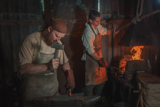 istock Two blacksmiths work in an old rural forge. Traditional crafts 2168411859