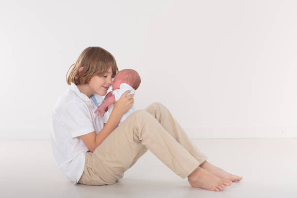12 year old boy hugs his sleeping newborn brother. Happy teenager lies with his baby brother on the bed.