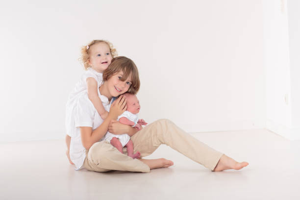 Siblings meet newborn baby. Child holding new infant brother for the first time. Kids visit mother in labor and delivery ward after birth of new baby. Sibling love. Family bonding.