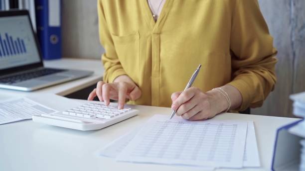 istock Businesswoman with yellow blues is using white calculator and taking notes in her office. Taxes and audit concept 2168443905
