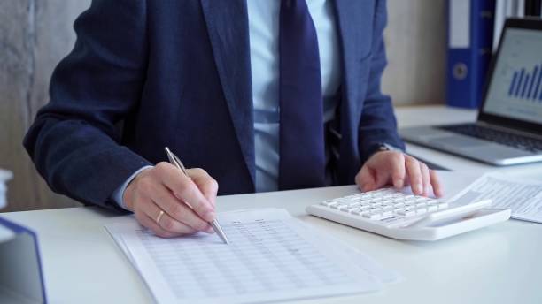 istock Businessman accountant with blue suit is using white calculator and taking notes with a silver pen. Taxes and audit concept 2168444724