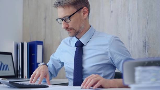 istock Male accountant with blue t-shirt concentrating while calculating costs and taking notes at his desk. Taxes, audit in business 2168446472