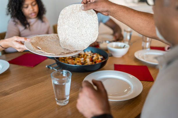 Thin flatbreads are being cooked on a large metal griddle over an open flame in an outdoor setting. The rustic cooking method and golden-brown texture highlight the authenticity and simplicity of traditional handmade food preparation.
