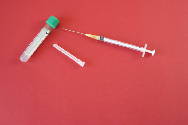 istock A hypodermic syringe and a plastic container with green lid for test and analysis on red background with copy space. 2168455734