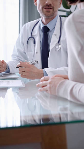 istock Doctor consulting patient. Male physician is gesturing above a clipboard while talking with a woman in a clinic, close up 2168456310