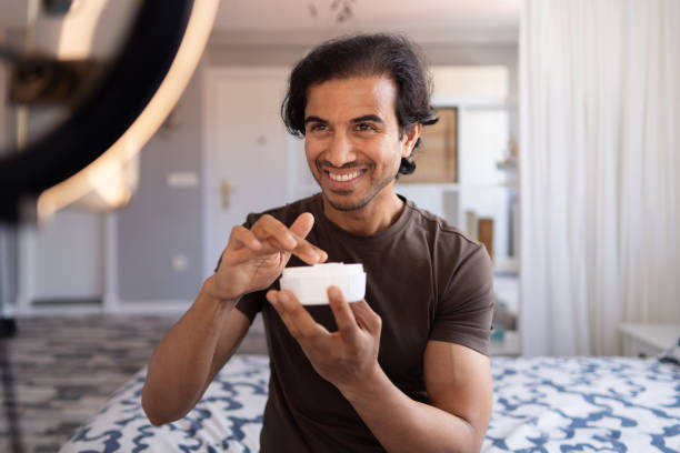 istock Male vlogger smiling while showcasing a moisturizer cream jar 2168470100