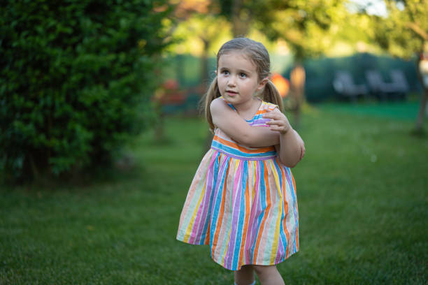 Cute little girl uninterested playing in the garden in a green grass backyard. Staycation boredom in summer.