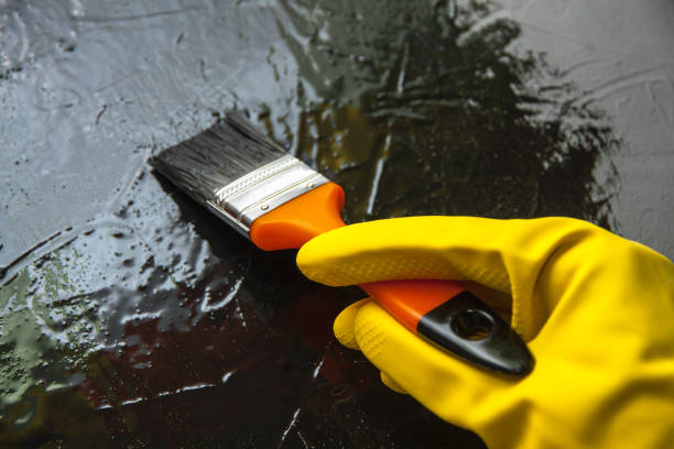 Hand with a brush in a yellow rubber glove, paints with black paint. The concept of creative design