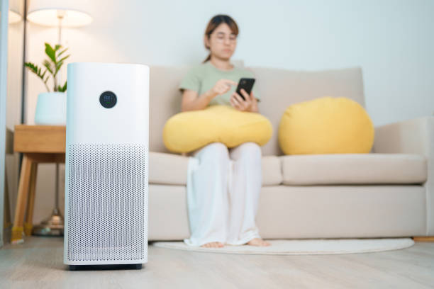 istock Air Purifier with woman relax and use smartphone on sofa. Purification system for filter and cleaning dust PM2.5 HEPA and virus in home. Allergy, Pure air, health, Wellness lifestyle and Air Pollution 2168492331