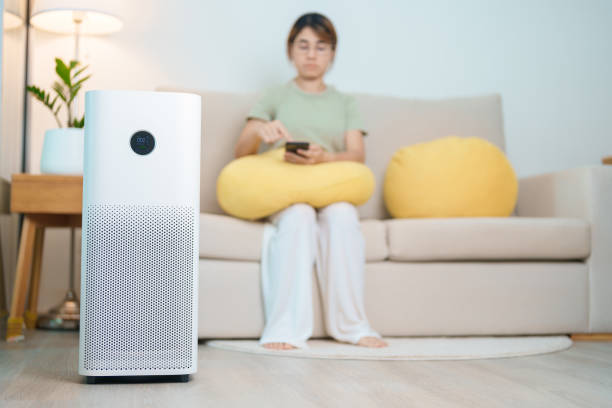 istock Air Purifier with woman relax and use smartphone on sofa. Purification system for filter and cleaning dust PM2.5 HEPA and virus in home. Allergy, Pure air, health, Wellness lifestyle and Air Pollution 2168492332