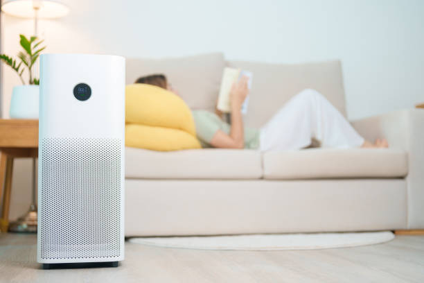 istock Air Purifier with woman read and relax on sofa. Purification system for filter and cleaning dust PM2.5 HEPA and virus in home. Allergy, Pure air, health lifestyle, Wellness life and Air Pollution 2168492335