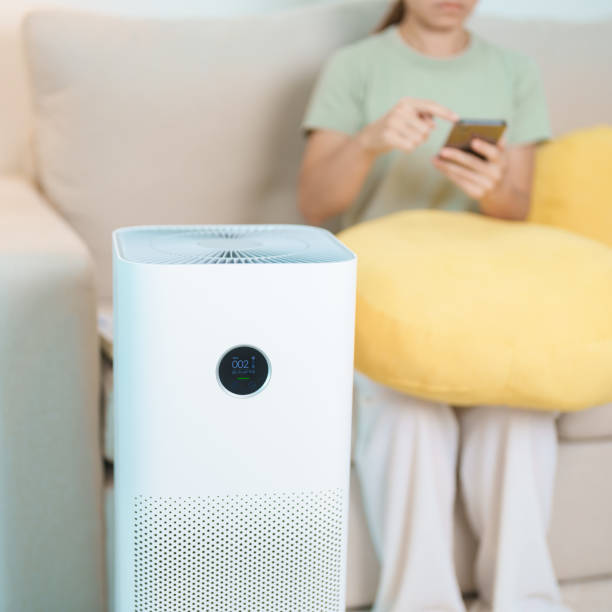 istock Air Purifier with woman relax and use smartphone on sofa. Purification system for filter and cleaning dust PM2.5 HEPA and virus in home. Allergy, Pure air, health, Wellness lifestyle and Air Pollution 2168492340
