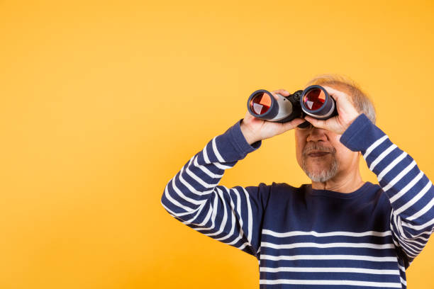 istock Portrait Asian smiling old man looking camera through binoculars studio shot isolated yellow background, senior man pensioner feeling surprised 2168494799