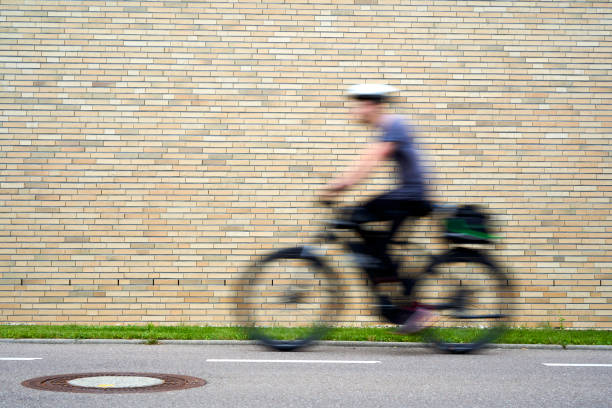 istock Person riding a bicycle in motion, captured with a blurred effect against a brick wall background, creating a sense of speed and movement. 2168497005