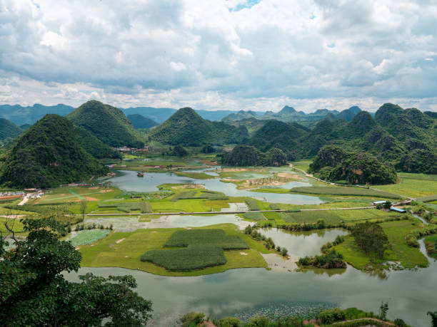 High angle view of green farmlands between rivers and mountain range in sunny cloudy day at Puzhehei, Yunnan, China. Aerial view landscape of Chinese villages, travel concept, go everywhere.
