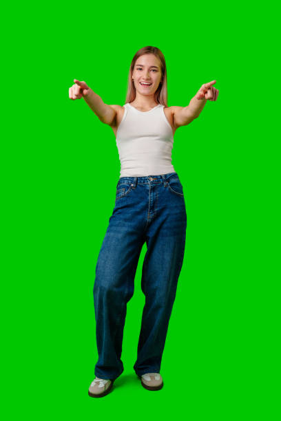 istock Young Woman Points to Camera While Smiling in Front of Green Screen 2168504543