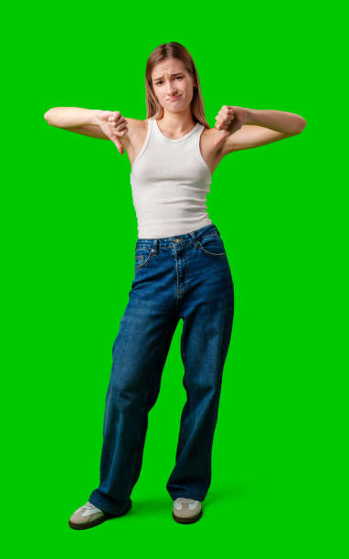 istock Young Woman Gives Thumbs Down While Standing Against Green Screen 2168504616