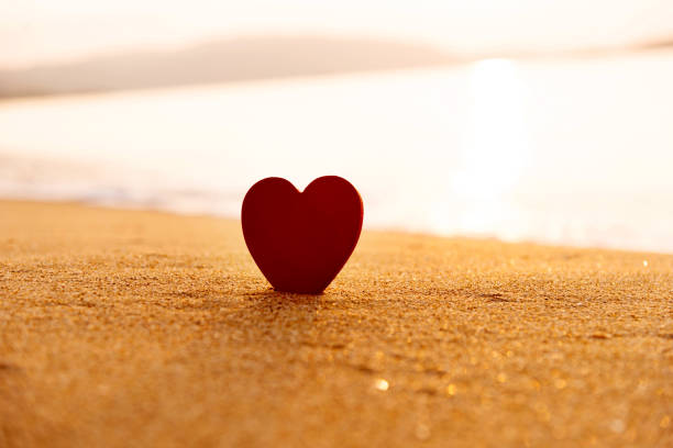 Red heart shape on the beach at sunset.