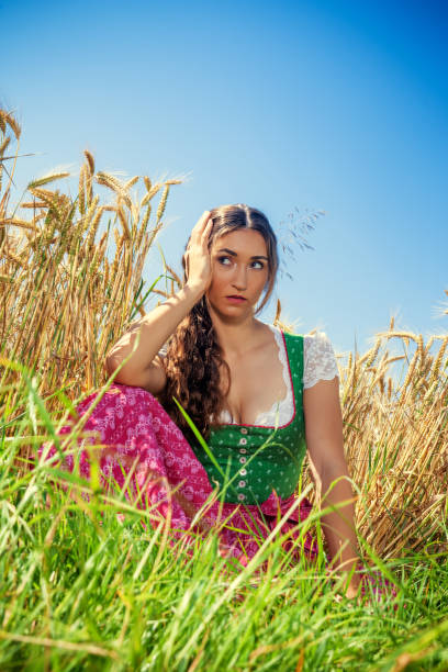 A beautiful young woman in a summer dress with a floral pattern next to a wooden well in a village. Shooting on a sunny summer day in the countryside