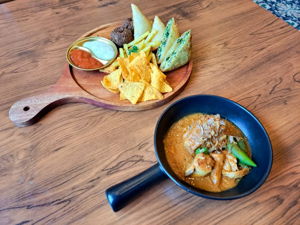 Prata Curry Dujjaj Serving Roti Prata With Chicken Curry Dish. Snack Mix Platter With Fried Sambosa Cheese Samosa, Mutabbaq, Falafel, Tortilla Chips And French Fries Serving With Spicy Sauce And Mayonnaise Sauce. Middle Eastern Food Menu. prata curry dujjaj sirviendo roti prata con plato de pollo al curry. plato de mezcla de bocadillos con queso sambosa frito, samosa, mutabbaq, falafel, chips de tortilla y papas fritas servido con salsa picante y salsa mayonesa. menú de comida de oriente m