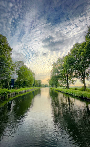 A tranquil view of a calm river flanked by lush trees under a picturesque sky, evoking peaceful imagery