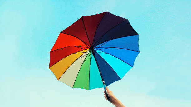 istock Female hands holding bright colorful multicolor umbrella on blue sky background 2168526106