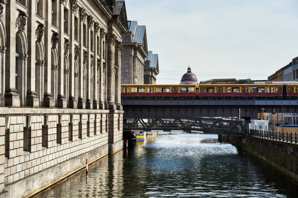 istock Yellow metro in Berlin stopped over a bridge on the river Spree with the castle dome standing out. Historical old building by the canal with the subway standing by on a bridge. Berlin tourism concept 2168530114