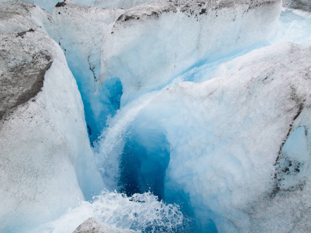 A deep ice crevasse within Mendenhall Glacier, Alaska, showcasing clear water and vibrant blue ice in the depths, emphasizing the natural glacial formation.