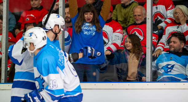 Excitement and Celebration in the Stands A female fan in a blue shirt and a young girl cheer enthusiastically as they celebrate with hockey players on the ice. The players in blue and white uniforms acknowledge the fans, creating a moment of connection. The background shows other fans, mostly in red jerseys, displaying mixed reactions, with some smiling and others showing different emotions. red hockey jersey stock pictures, royalty-free photos & images