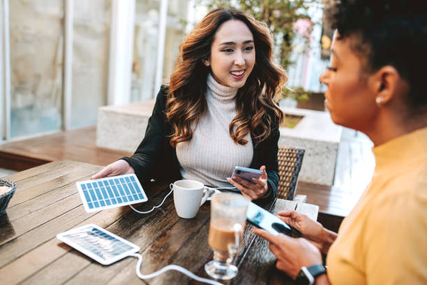 istock Two friends in coffee shop charging cell phone on portable solar panel board 2168546651