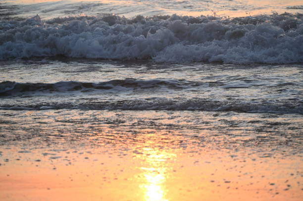 Golden light shining on wet sand after a wave retreats back into the ocean on the beach