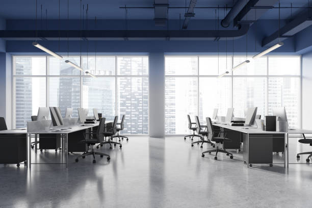 istock Dark coworking interior with pc desktops on tables in row, panoramic window 2168579953